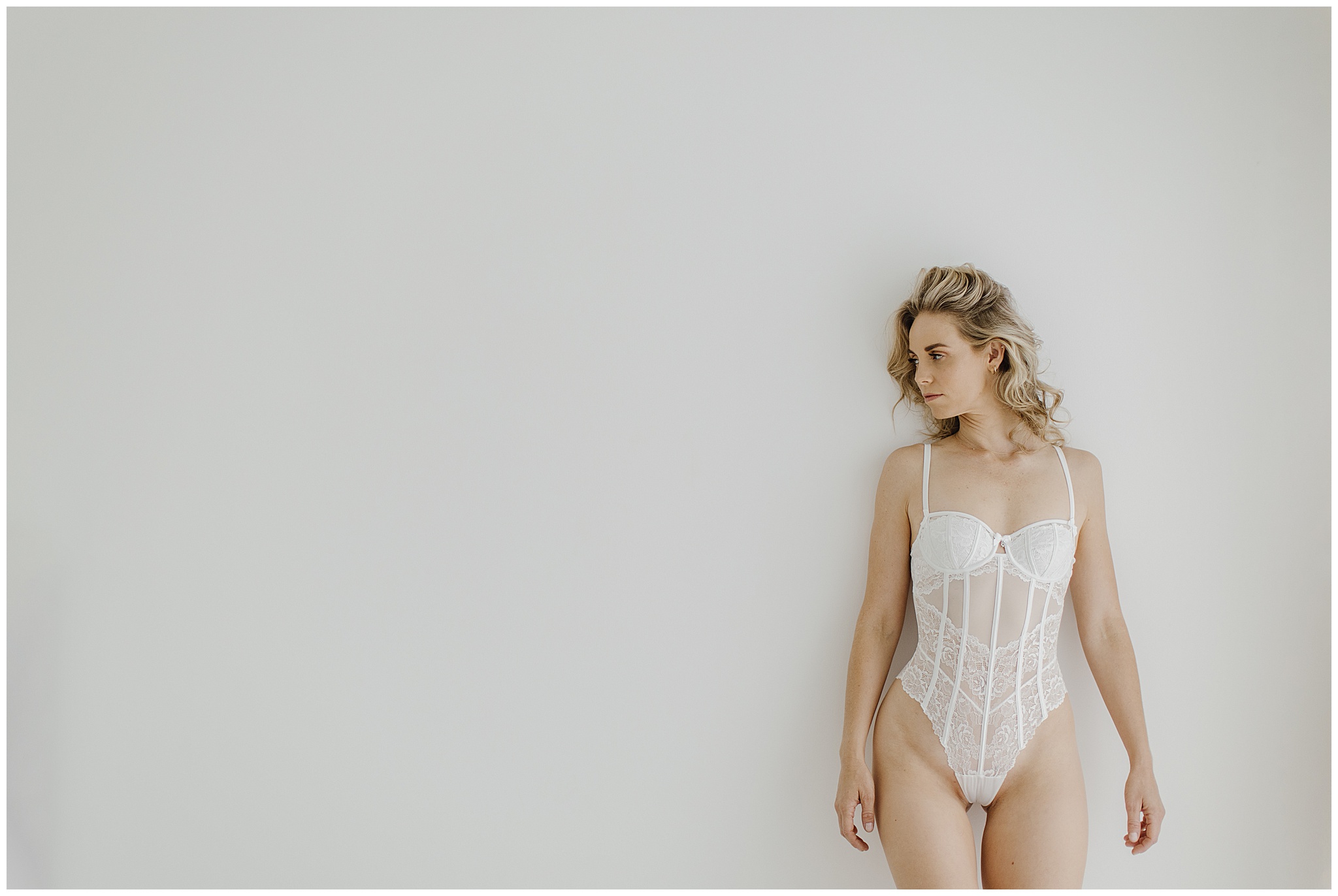 Stunning woman with blonde hair and wearing white bodysuit lingerie for boudoir photography session with Alyce Holzy Boudoir.